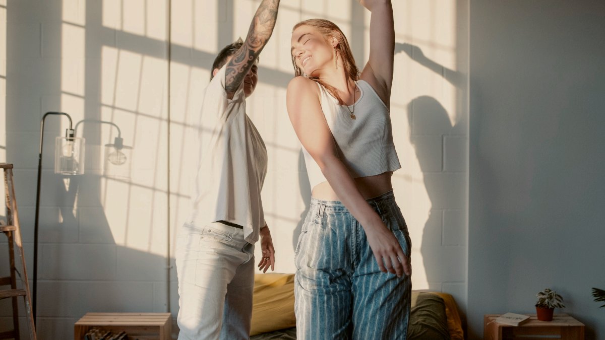
a woman and man dancing on top of a bed with sunlight coming through a window by jayson hinrichsen
