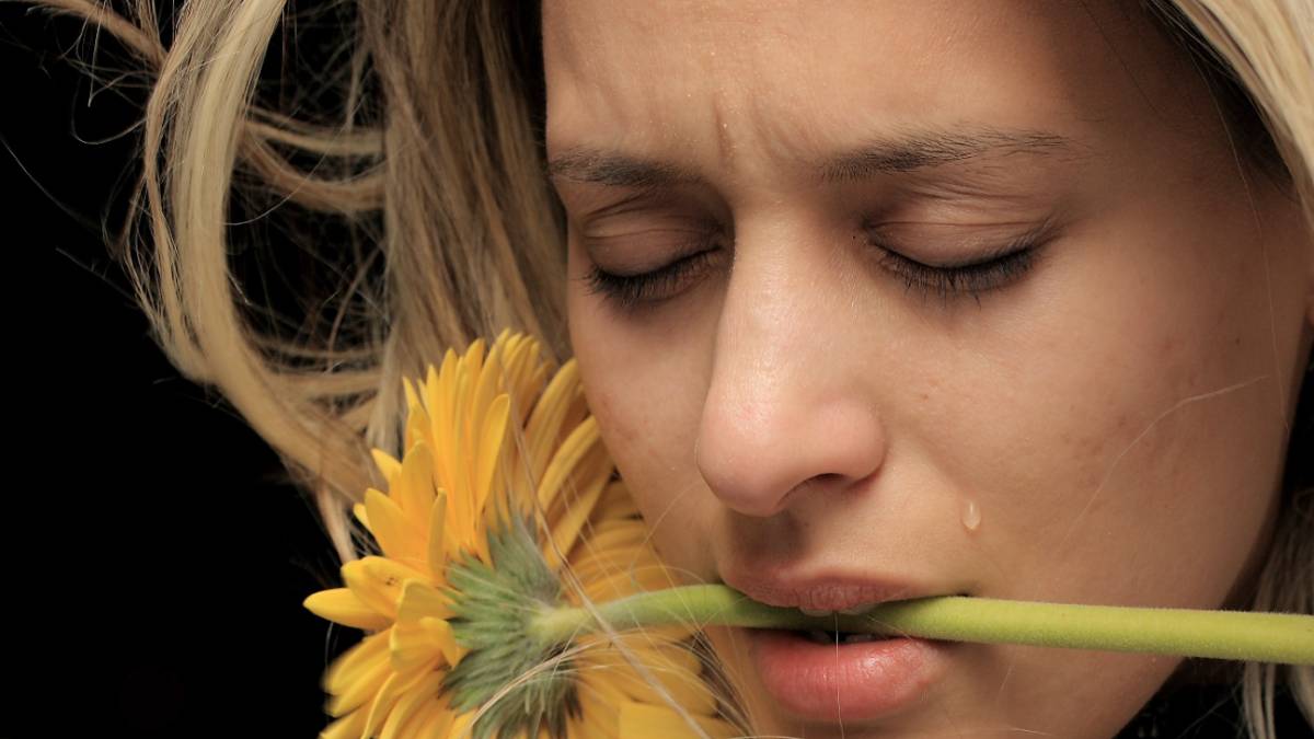 
a woman crying and holding a flower in her mouth because she is grieving
