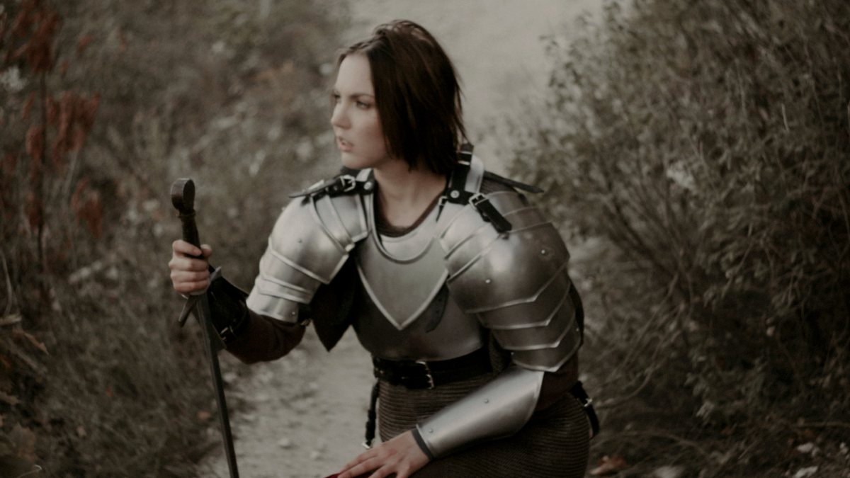 
a-woman-dressed-as-a-knight-kneeling-on-a-path
