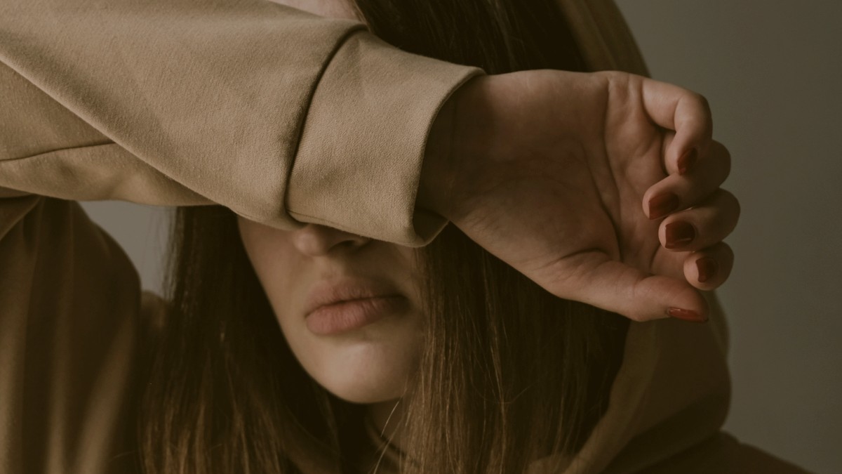 
a woman in a brown hoodie covering her eyes with her arm
