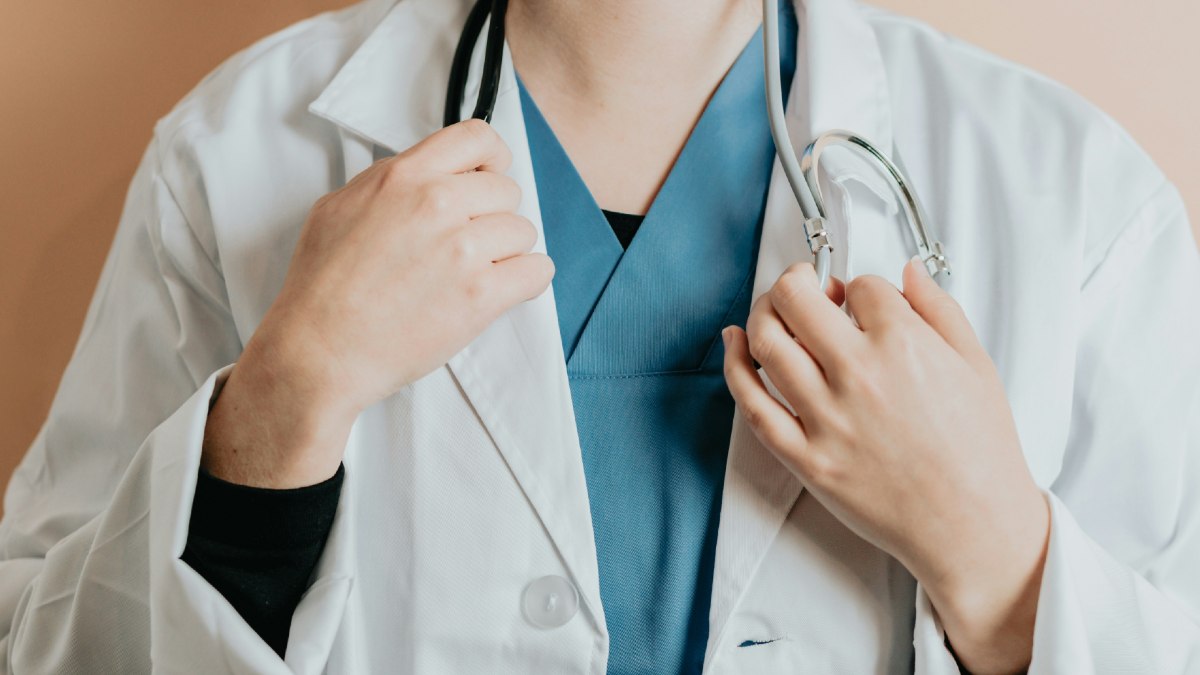 
a woman in a white lab coat and blue scrubs holding a stethoscope by ac
