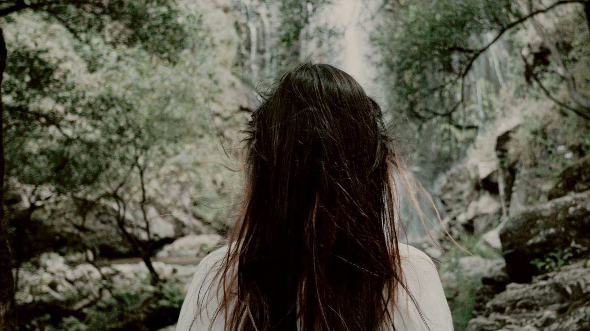 
a woman in a white shirt standing in front of a waterfall by AC
