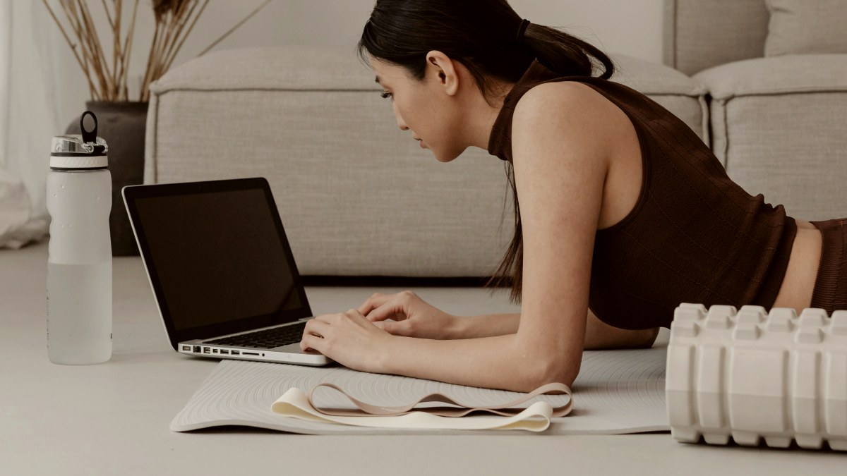 
a woman in activewear laying on the floor using a laptop
