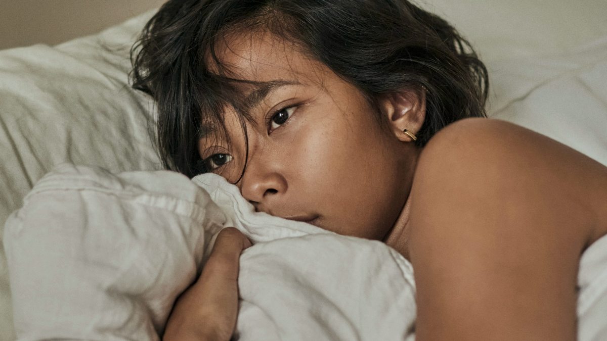 
a woman laying in bed with a white comforter looking sad by Daniel Martinez
