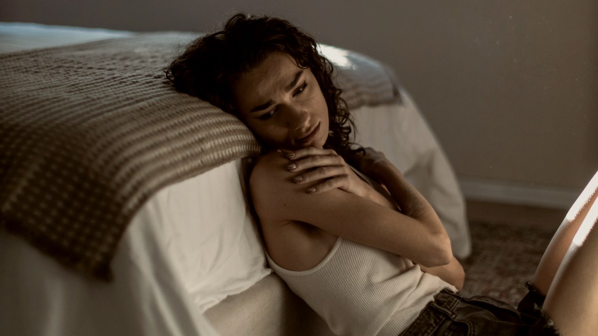 
a woman laying on top of a bed next to a window hugging herself by Meg Aghamyan
