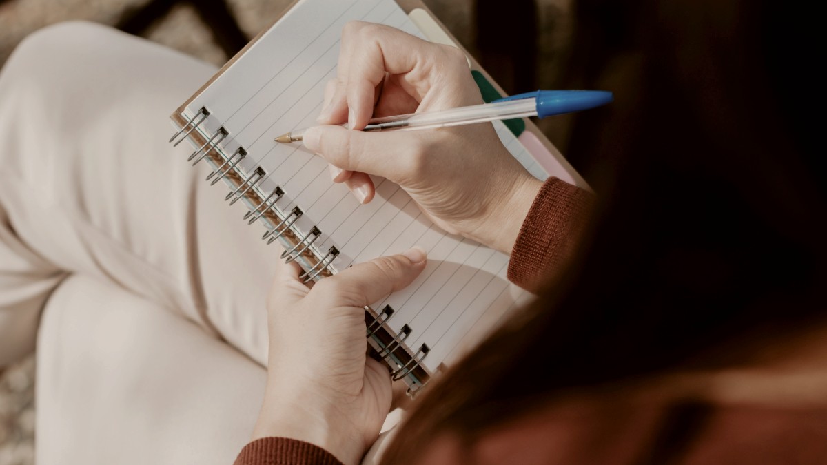 
a-woman-sitting-at-a-table-writing-on-a-notebook
