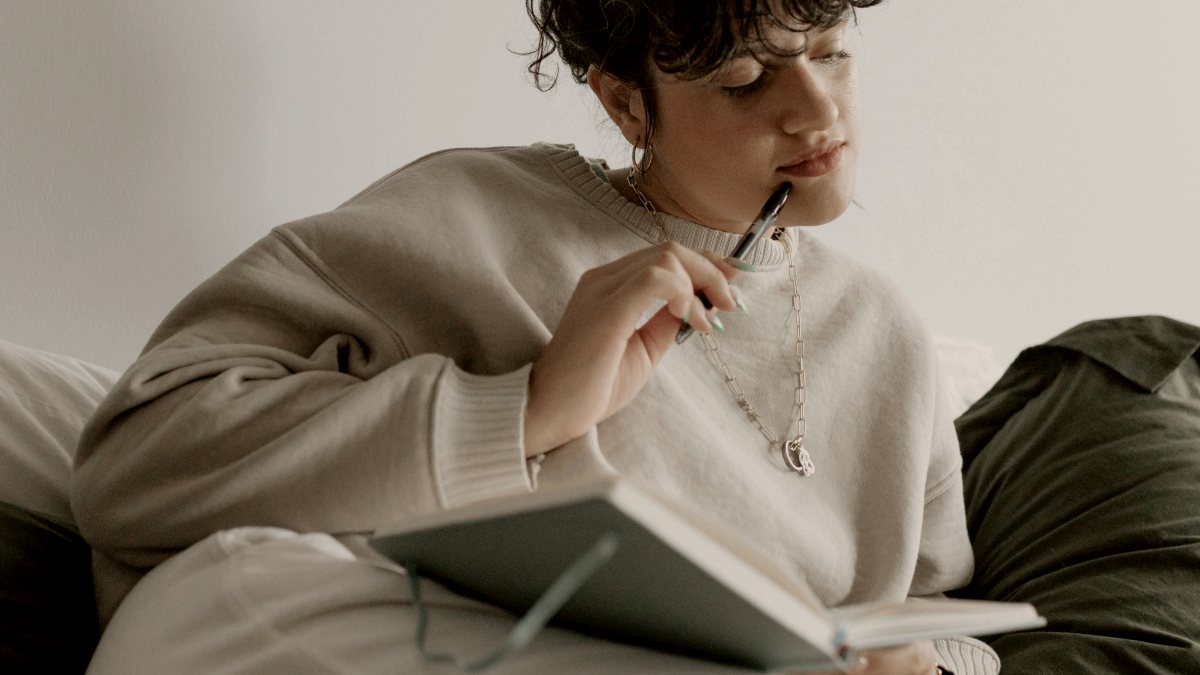 
a woman sitting on a bed with a notebook in her hand
