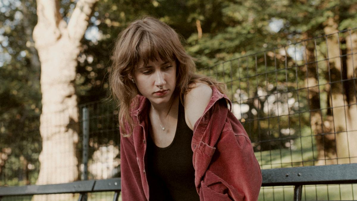 
a woman sitting on a bench in a park wearing red jacket by Victoria Romulo
