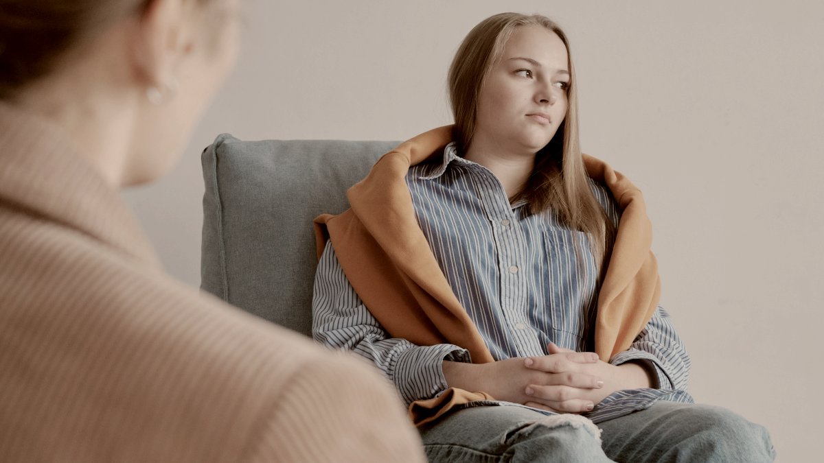 
a woman sitting on a couch talking to another woman in therapy by andrej lisakov
