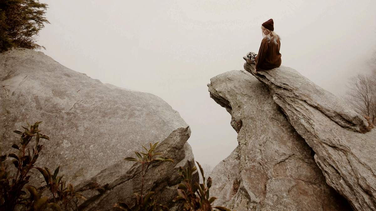 
a-woman-sitting-on-a-high-cliff
