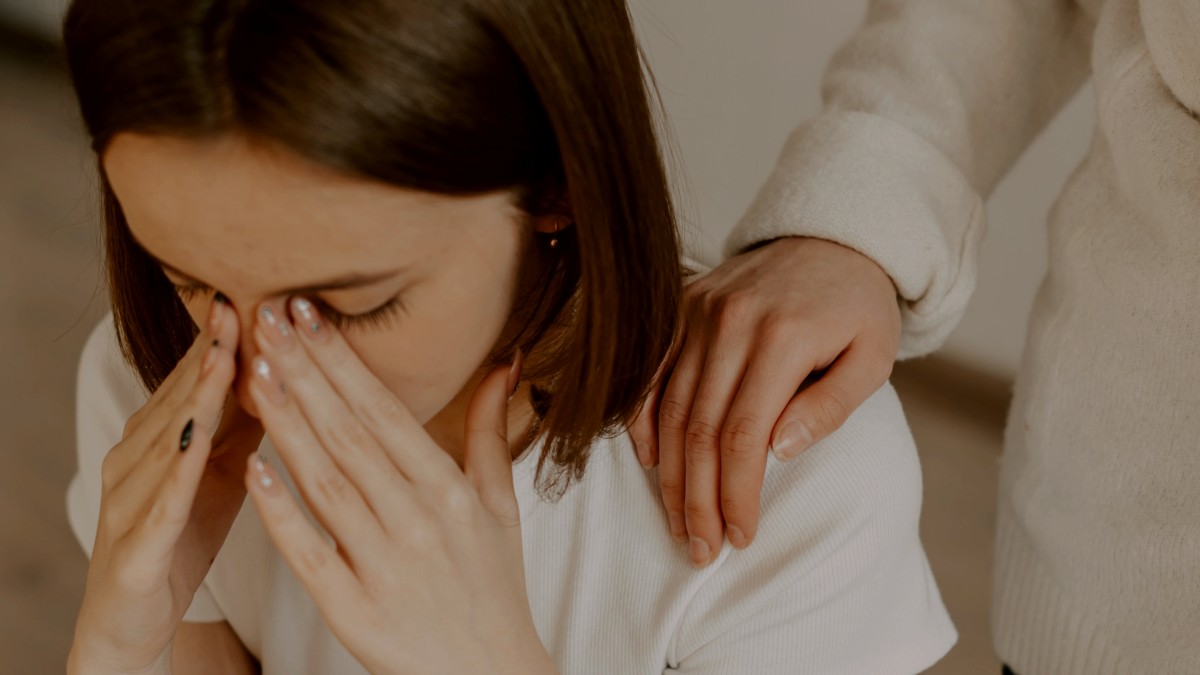 
a woman sitting on the floor covering her face as her partner comforts her
