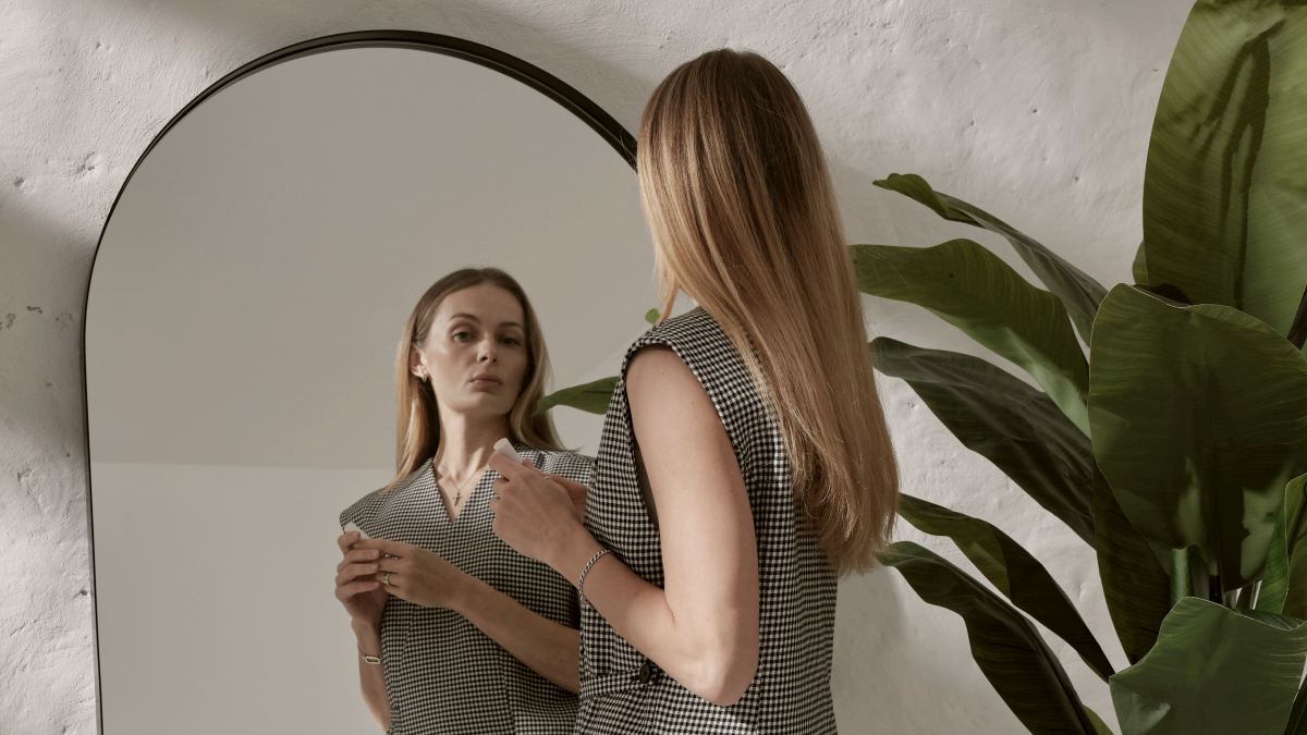 
a woman staring at her reflection in a modern mirror against a white wall

