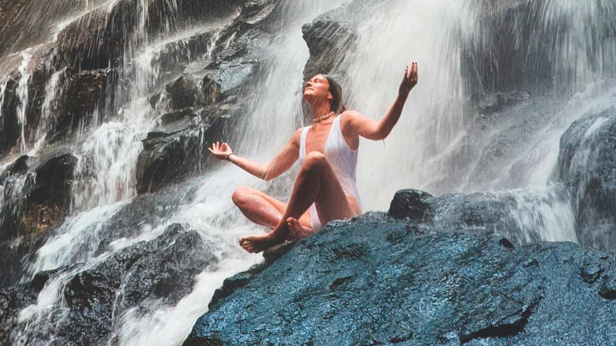 
a woman under a waterfall trusting her karmic beliefs
