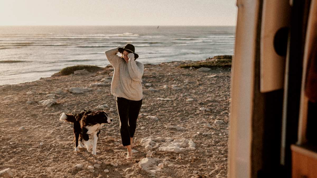 
a-woman-walking-a-dog-on-a-beach-next-to-a-van
