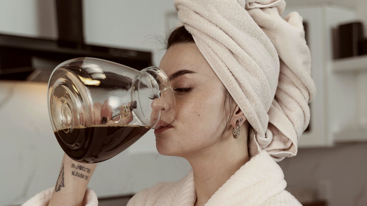 
a woman with a towel on her head drinking from a coffee pitcher
