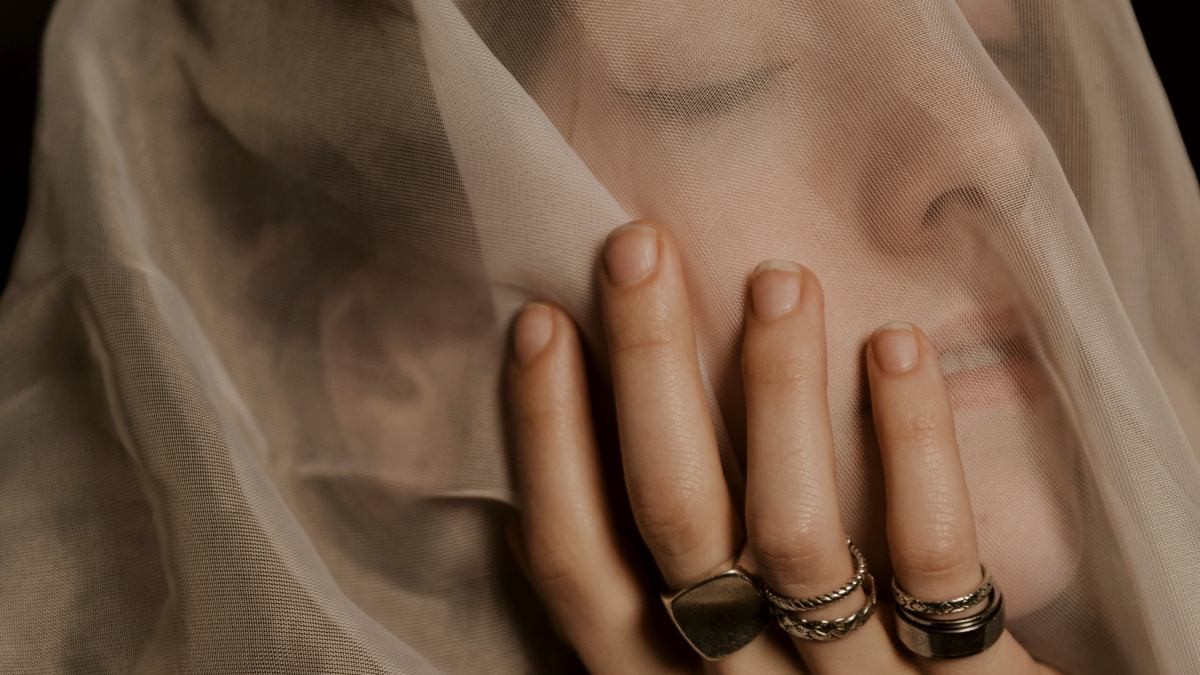 
a woman with a veil covering her face and rings on her fingers
