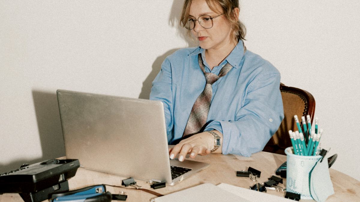 
A woman works on her laptop at a messy desk
