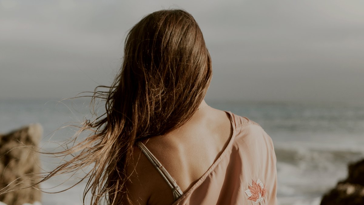 
Back of a woman standing along a rocky beach with hair blowing in the breeze by Curated Lifestyle
