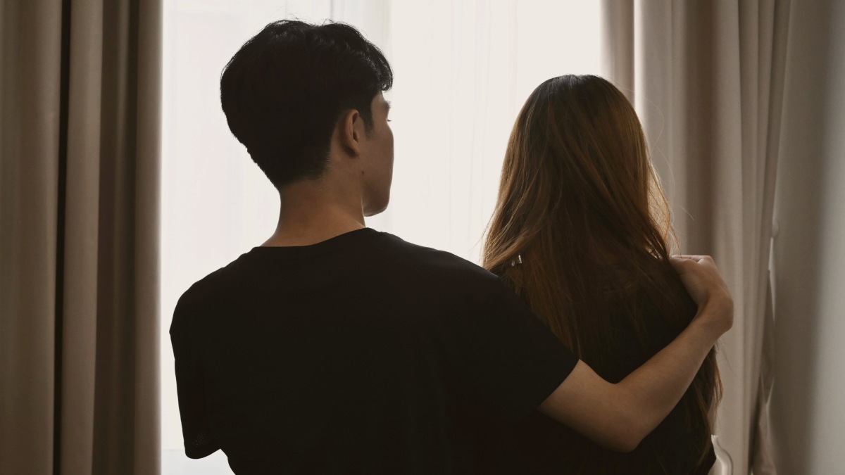 
Back view of young man embracing his wife and sitting in bed room
