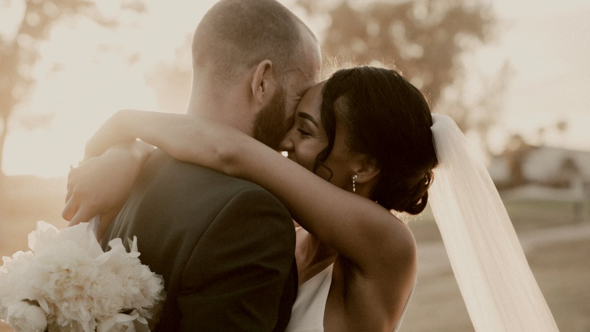 
bald man in black suit embracing woman in white wedding dress holding a bouquet by Jakob Owens
