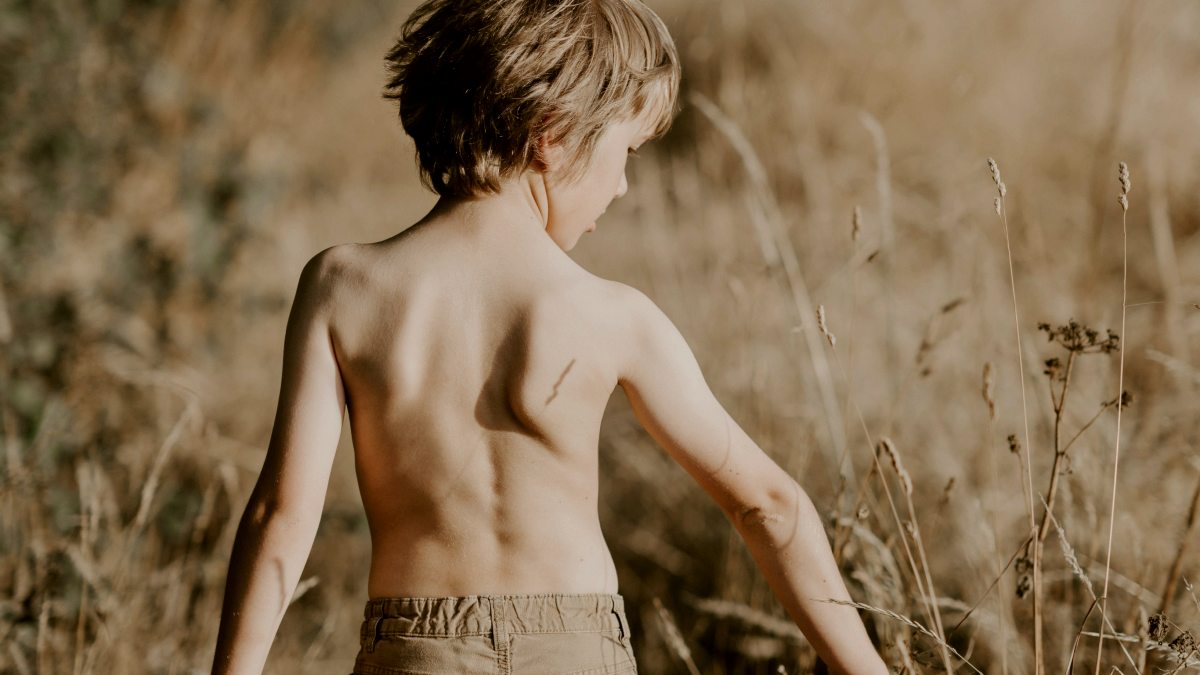 
boy walking through a field holding onto brown grass
