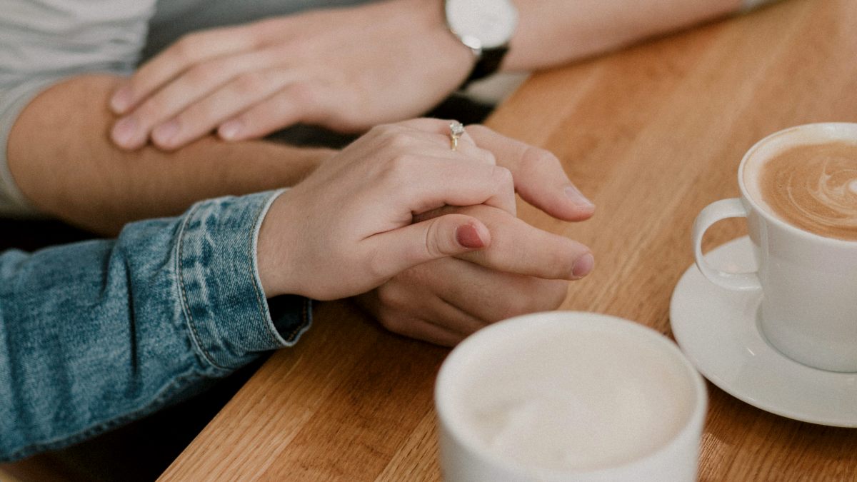 
close up of man and woman holding hands with coffee cups on wooden table by priscilla du preez
