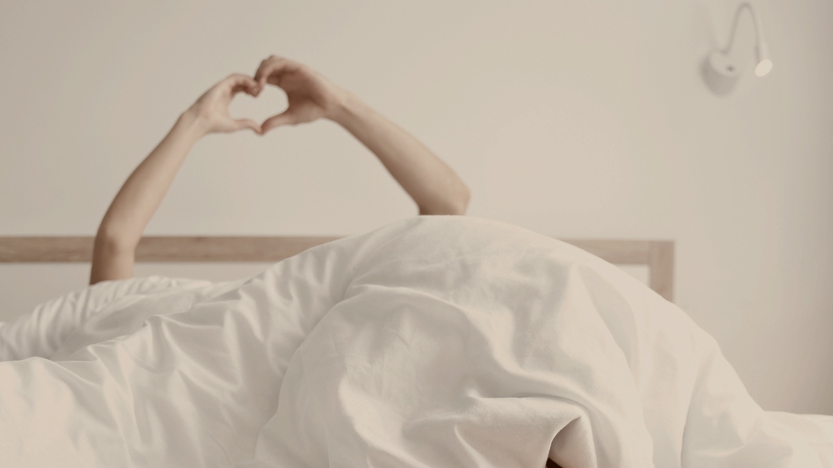 
Cropped photo of newly wedded couple making a heart shape with their hands in bed by Getty Images
