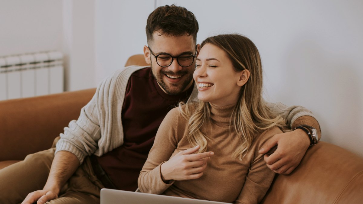 
Handsome young couple using laptop together while sitting on sofa at home
