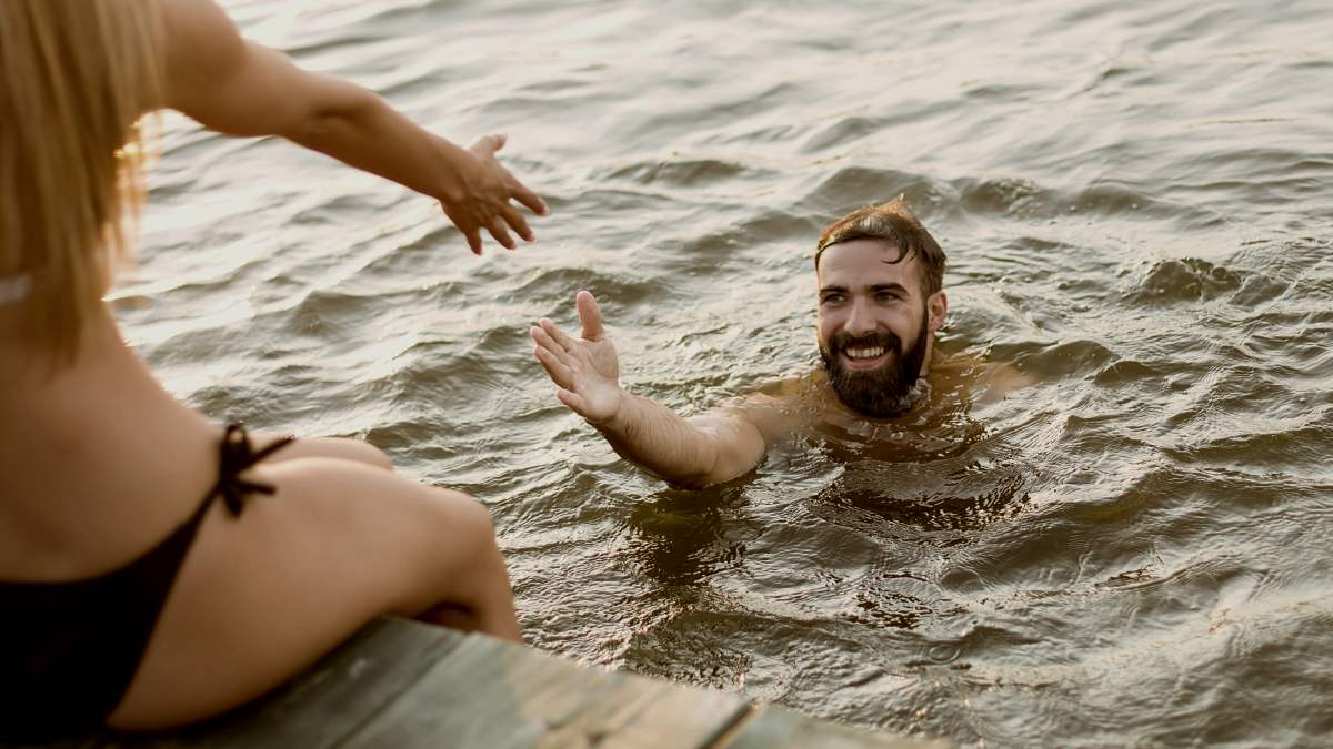 
Happy young couple enjoying while woman sitting on pier and man swimming in the lake
