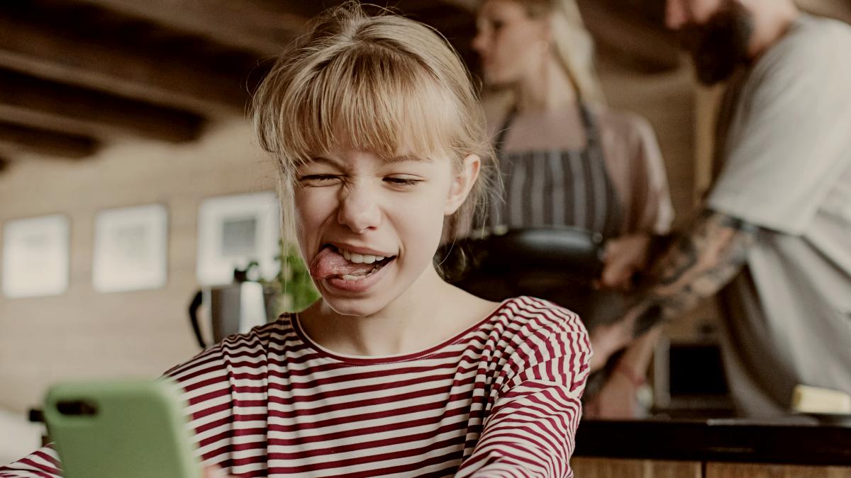 
Little girl making a grimace and taking selfie when her parents cooking indoors by getty images
