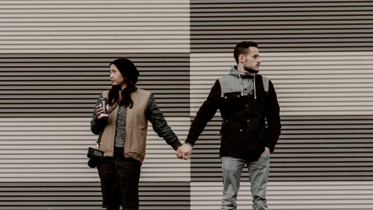 
man and woman holding each other's hands by a painted wall
