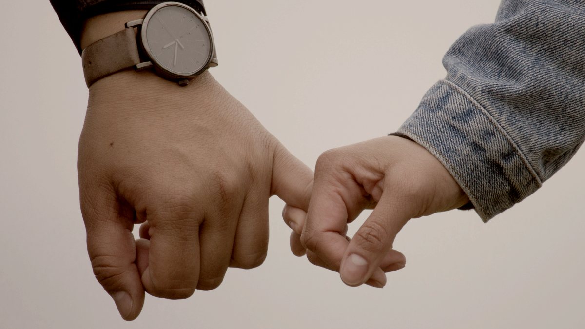 
man and woman in denim jacket holding pinkies together outside by Ryan Franco

