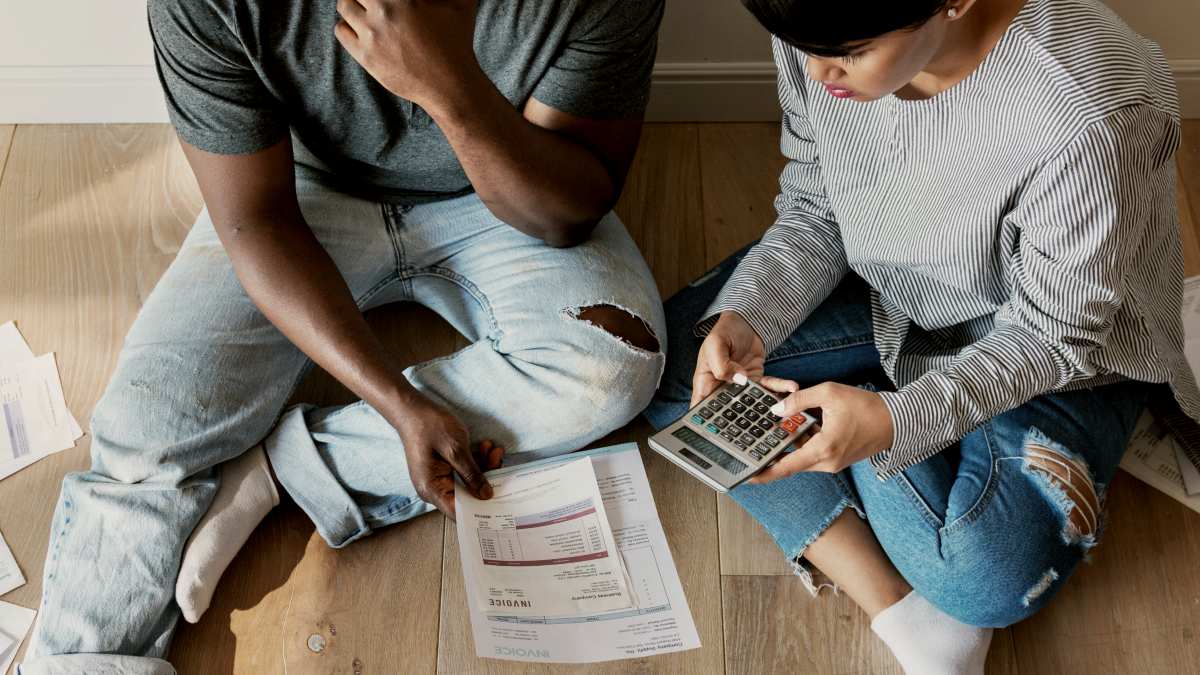 
Man and woman on the floor surrounded by bills and using calculator by curated lifestyle 

