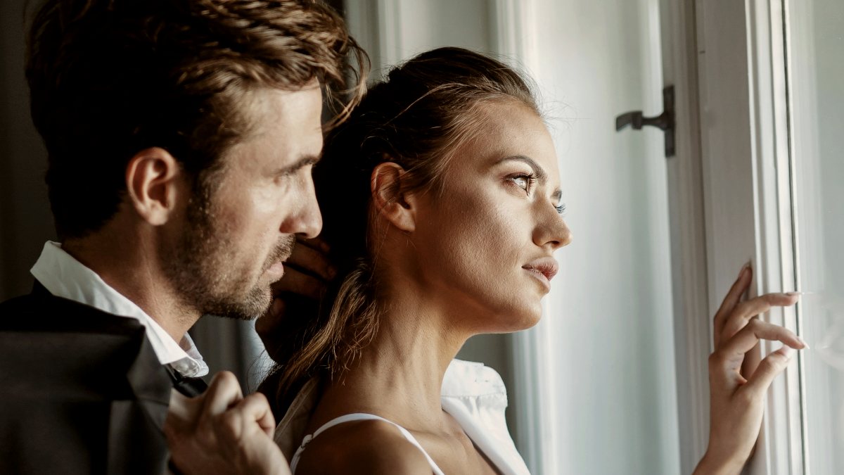 
man and woman staring out the window together looking pensive
