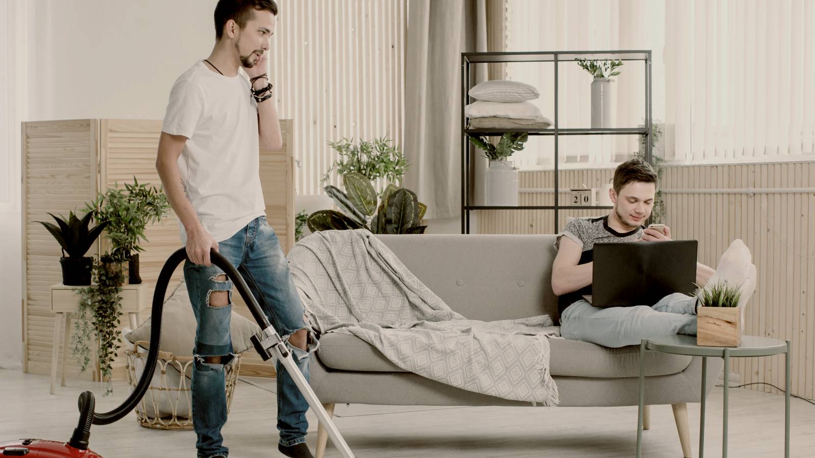 
man cleaning living room, another man holding the laptop, sitting on sofa by Getty Images
