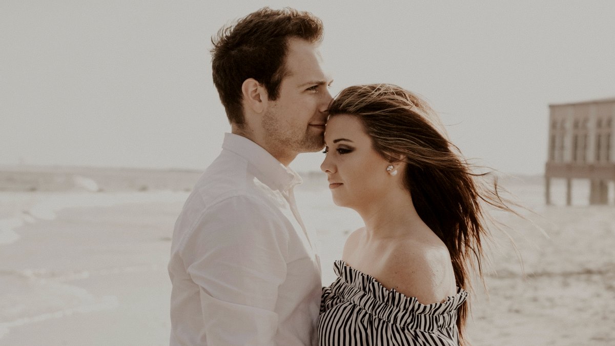 
man giving his partner a forehead kiss on the beach
