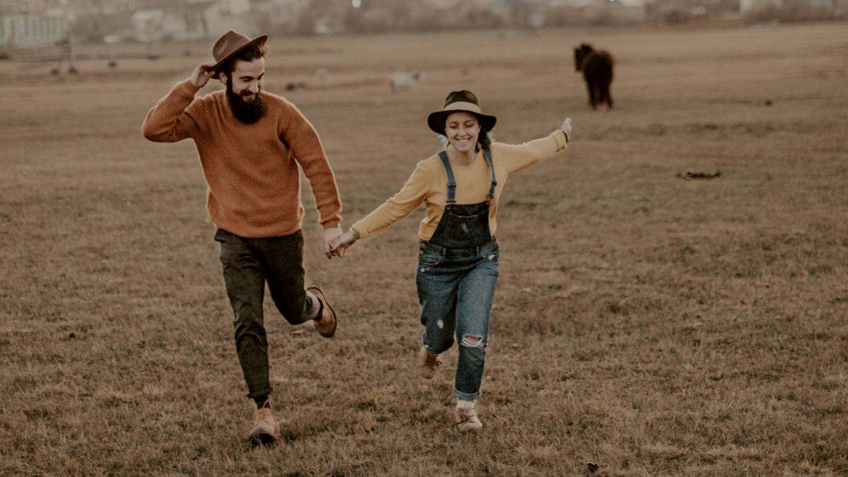 
man holding womans hand as they run together through a field
