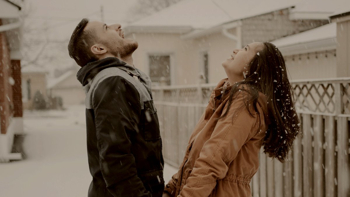 
man in black jacket and woman in brown coat standing on snow covered ground during daytime with faces turned to the sky by Andrik Langfield
