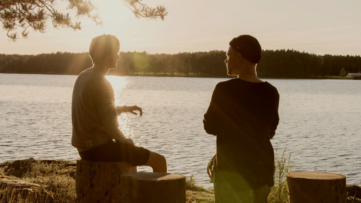 
man in black jacket standing beside body of water during sunset talking to man in beanie by Aarón Blanco Tejedor
