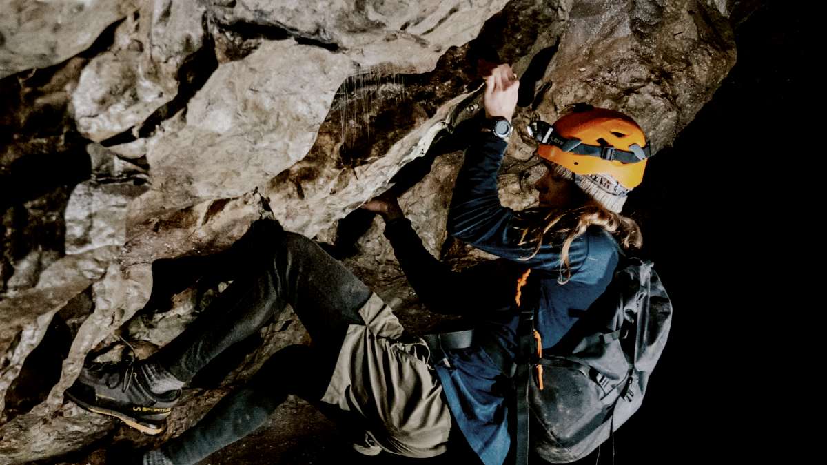
man in blue jacket and black pants climbing on rock in dark cave by Jason Gardner
