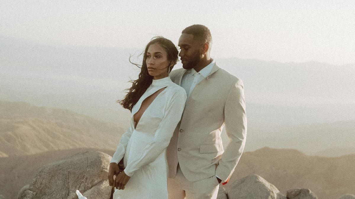 
man in white suit standing beside woman in white dress and high heels on rock during daytime
