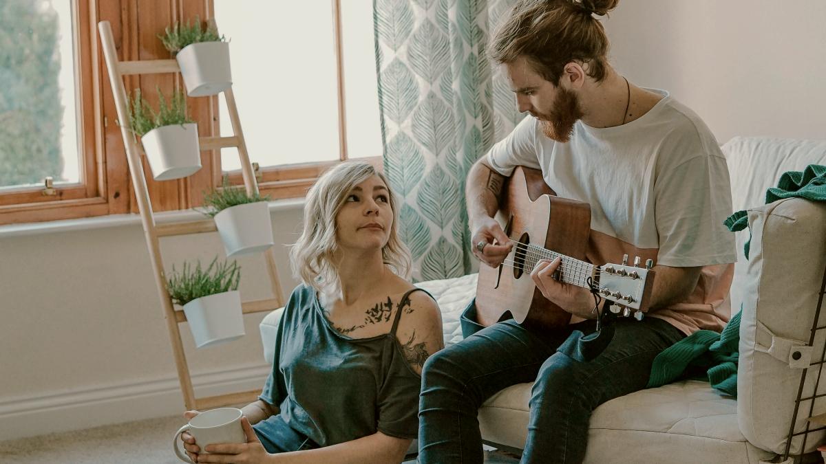 
man-playing-guitar-on-sofa-looking-at-his-girlfriend-on-the-floor
