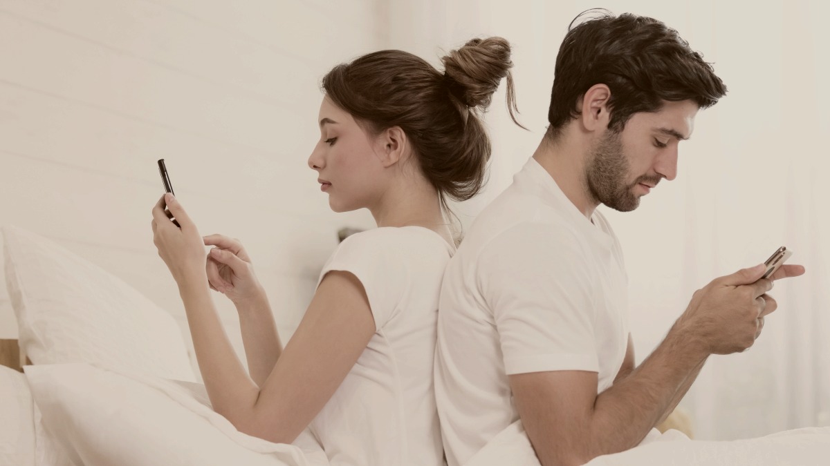 
Millennial couple in quarrel, lying in bed back to back, using cellphones by Getty Images
