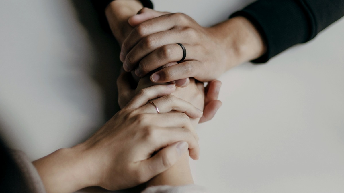 
person in black long sleeve shirt holding hands with woman in white long sleeves, both wearing wedding rings
