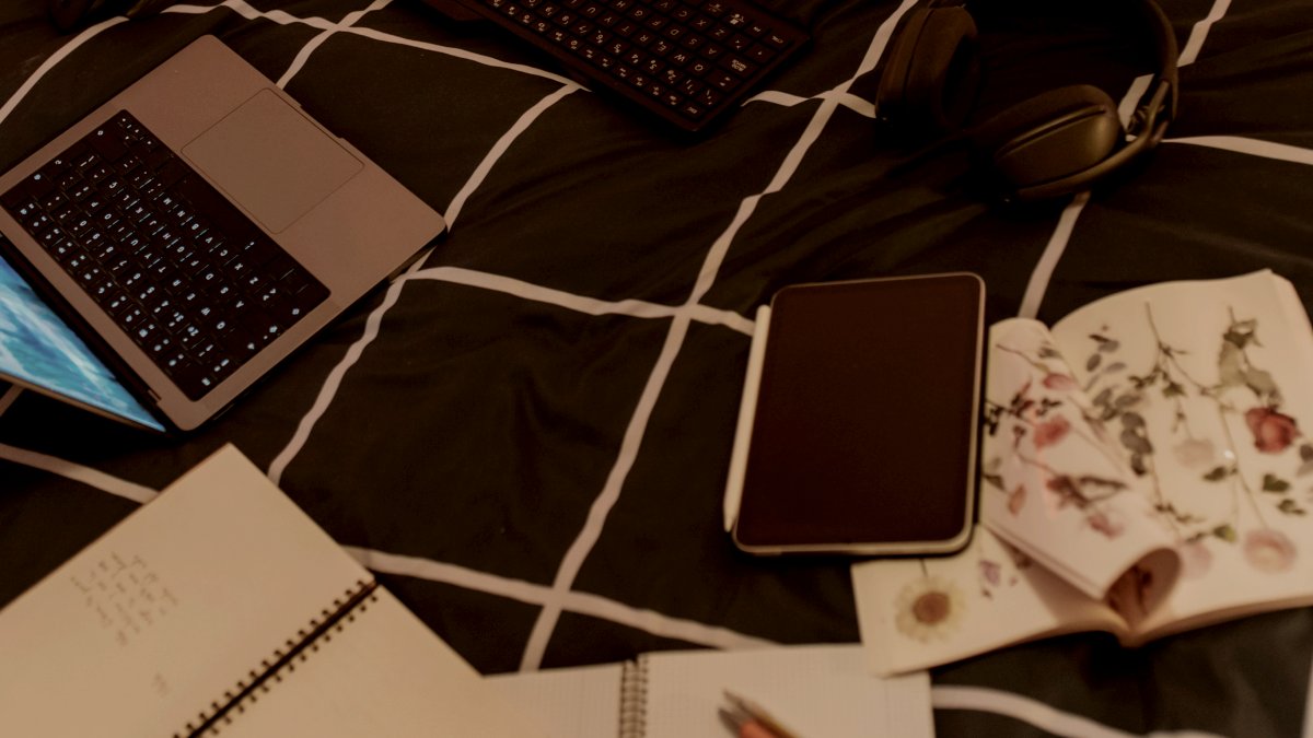 
Pizza and tech sprawl across a messy bed by Elena Helade
