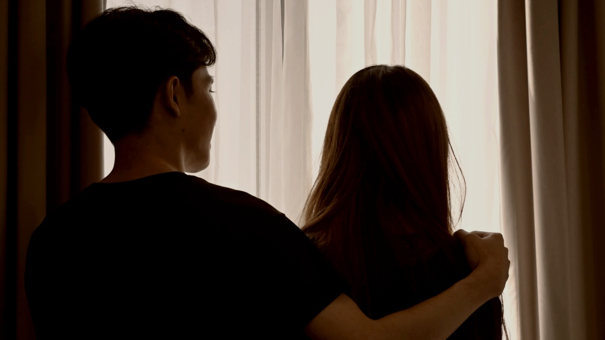 
Silhouette of young couple embracing and standing in living room opposite window at home by getty images

