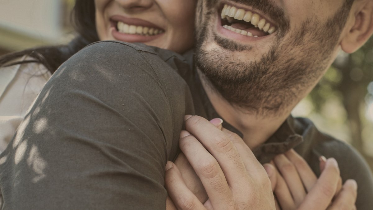 
Smiling young couple sitting in park, share a tender hug from behind by Getty Images
