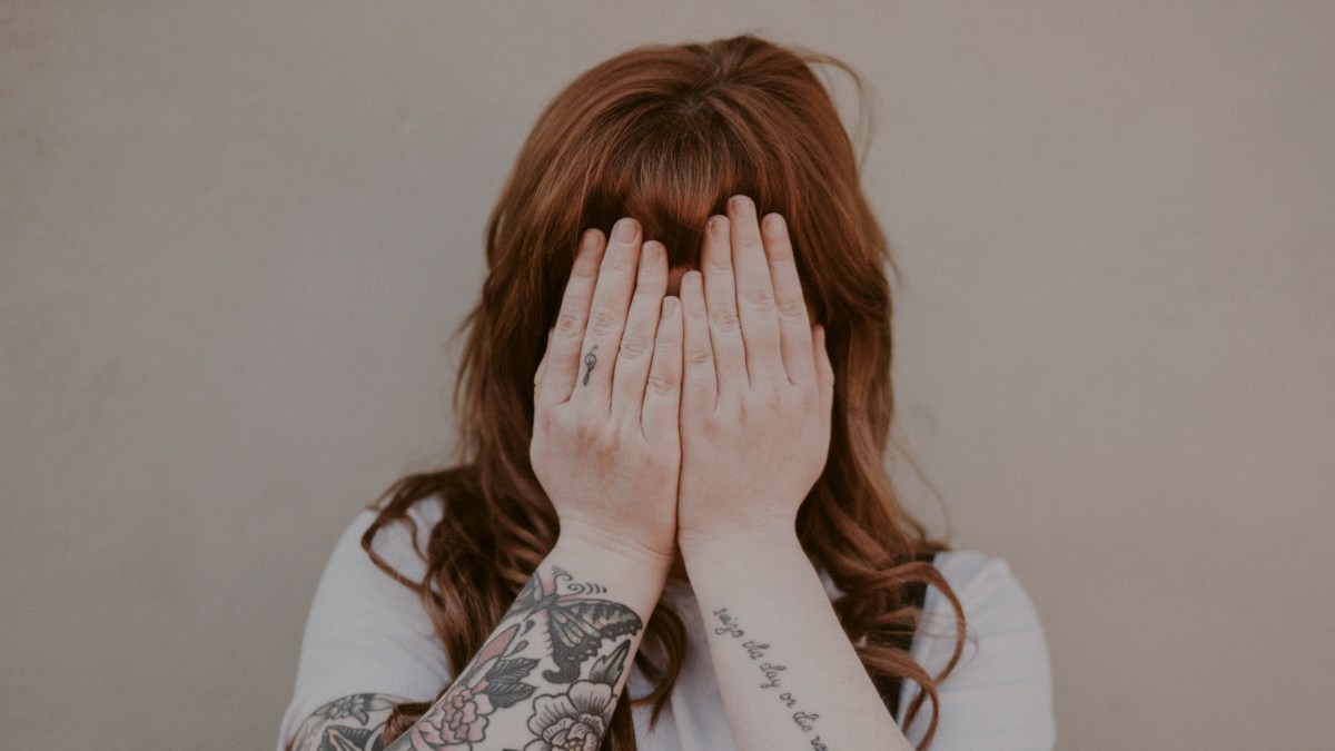 
tattooed woman covering her face in front of wall
