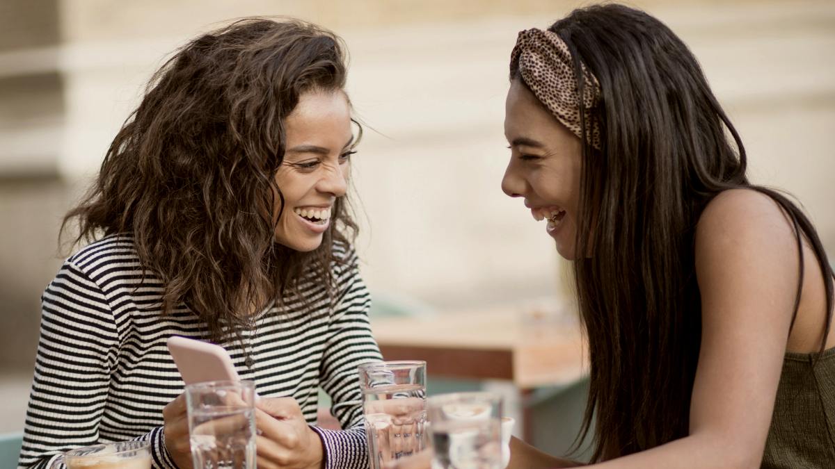 
Two women at café outdoors using smart phone by Getty Images
