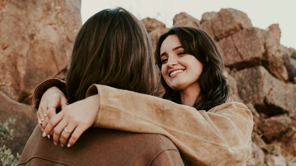 
Two women hugging each other in front of a mountain
